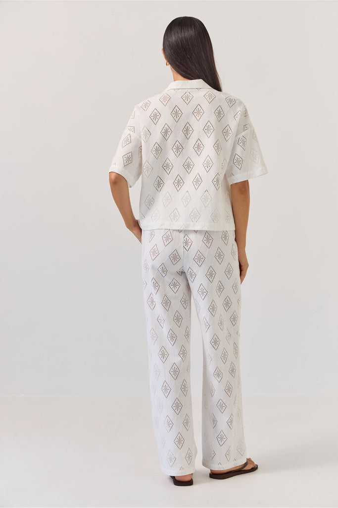 Woman wearing a white patterned matching embossed shirt and pant on a plain background