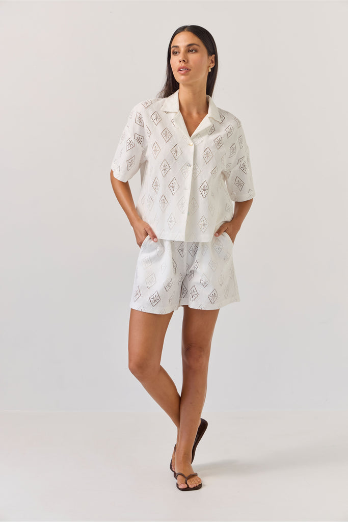 Woman wearing a white patterned matching embossed shirt and short on a plain background