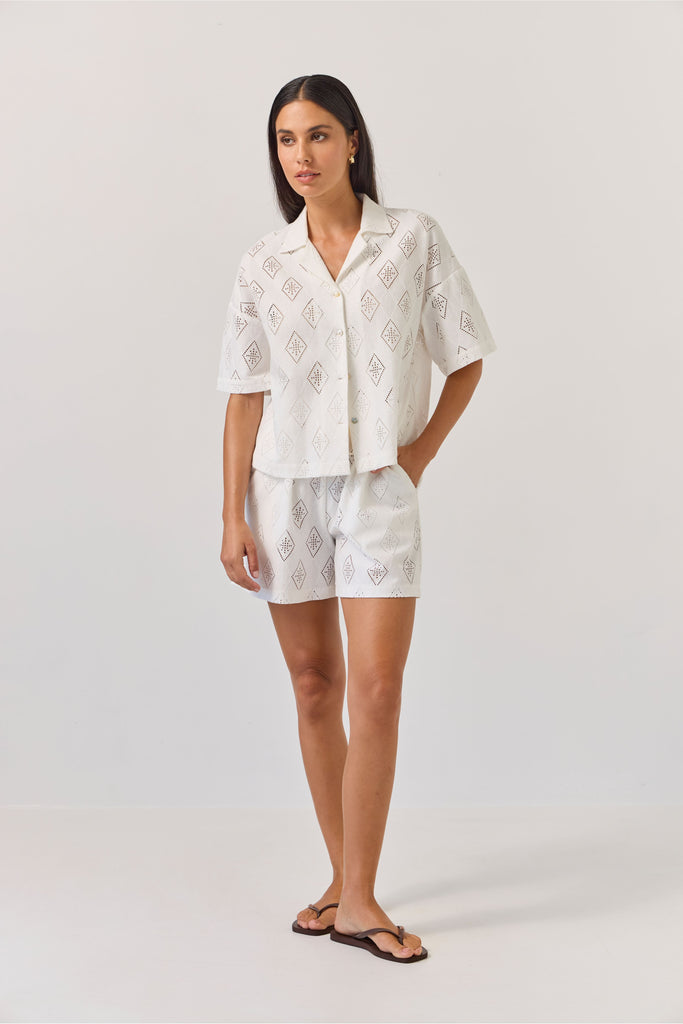 Woman wearing a white embroidered outfit on a plain background. Tuesday Label revere Top and Umpire Shorts in Diamond.