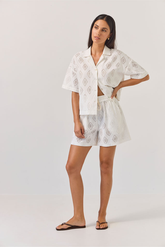 Woman wearing a white embroidered outfit on a plain background. Tuesday Label revere Top and Umpire Shorts in Diamond.
