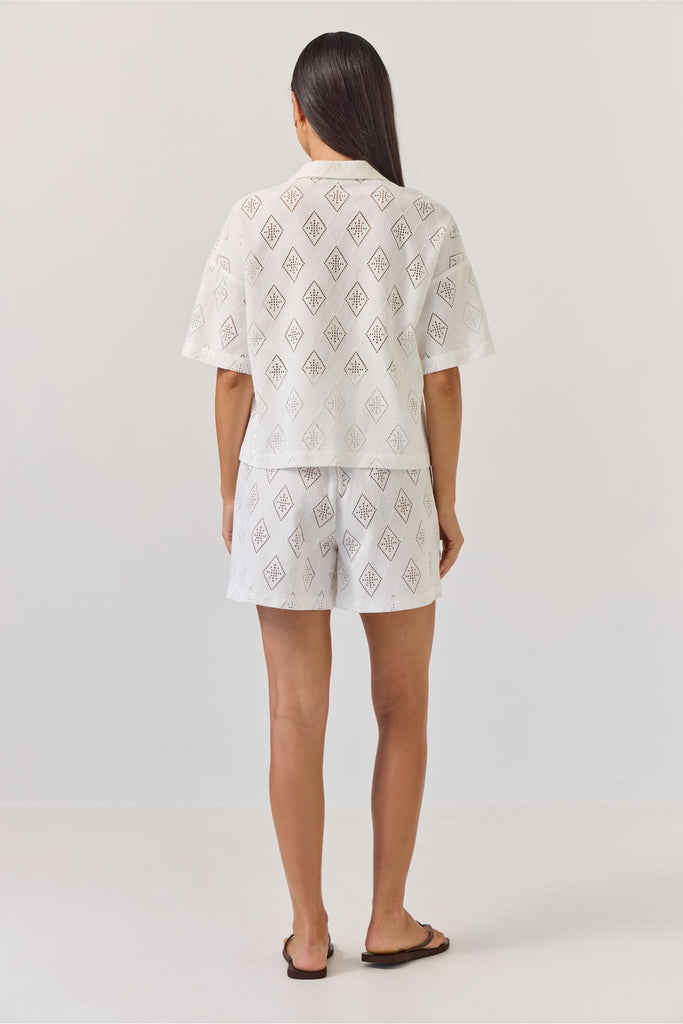 Woman wearing a white embroidered outfit on a plain background. Tuesday Label revere Top and Umpire Shorts in Diamond.