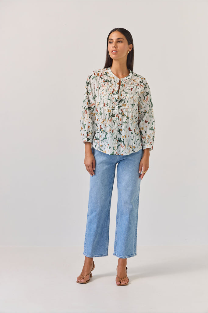 Woman wearing a floral blouse and blue jeans against a plain background. Tuesday Label Maeve Floral Top.