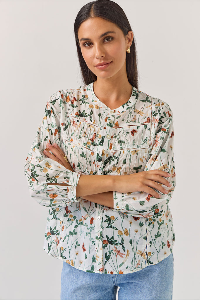 Woman wearing a floral blouse and blue jeans against a plain background. Tuesday Label Maeve Floral Top.