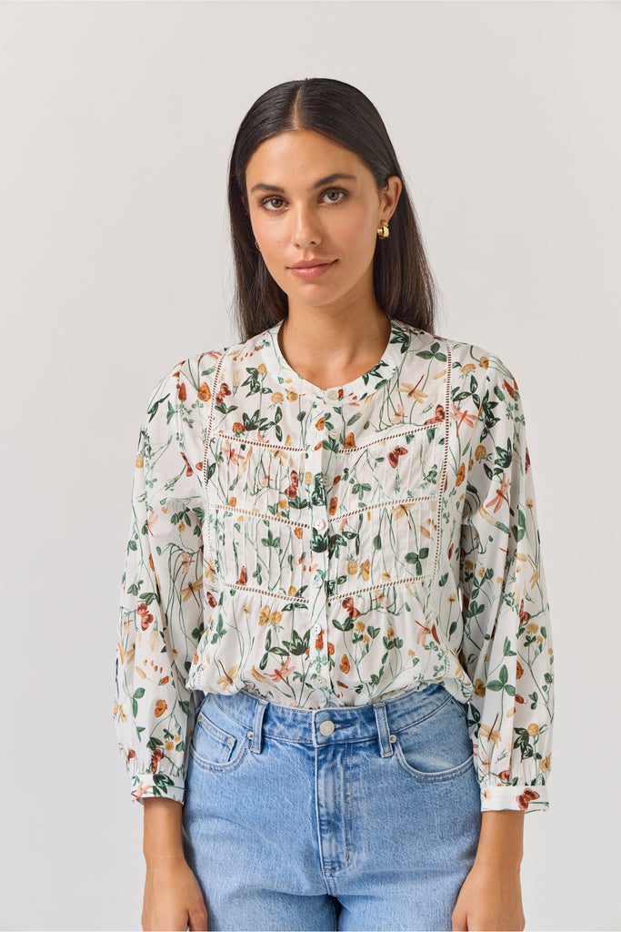Woman wearing a floral blouse and blue jeans against a plain background. Tuesday Label Maeve Floral Top.