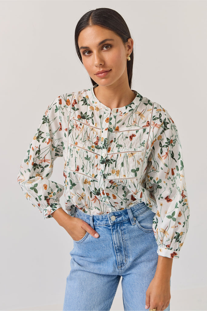 Woman wearing a floral blouse and blue jeans against a plain background. Tuesday Label Maeve Floral Top.