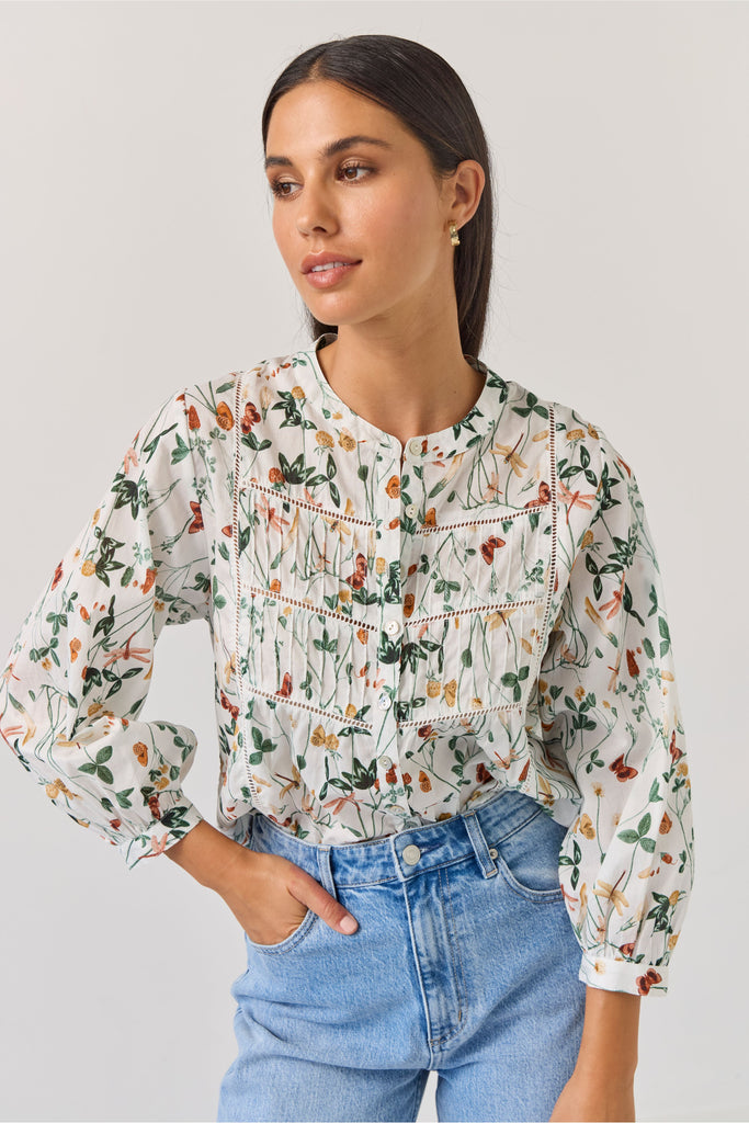Woman wearing a floral blouse and blue jeans against a plain background. Tuesday Label Maeve Floral Top.