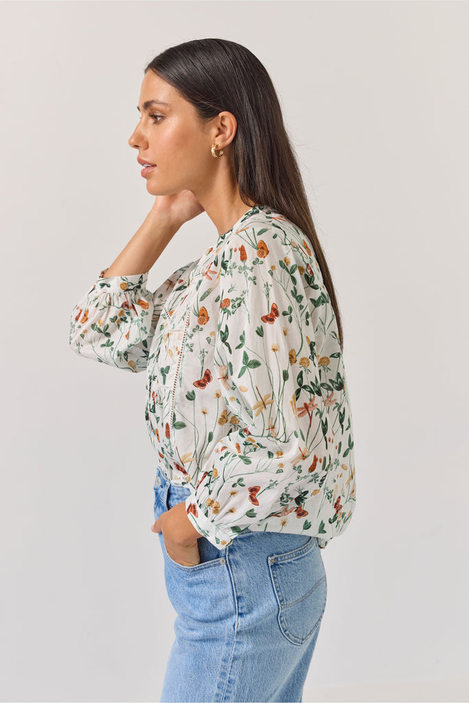 Woman wearing a floral blouse and blue jeans against a plain background. Tuesday Label Maeve Floral Top.