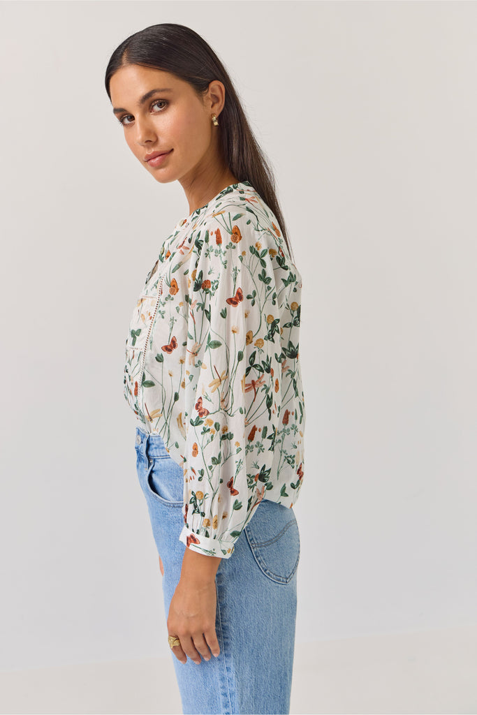 Woman wearing a floral blouse and blue jeans against a plain background. Tuesday Label Maeve Floral Top.