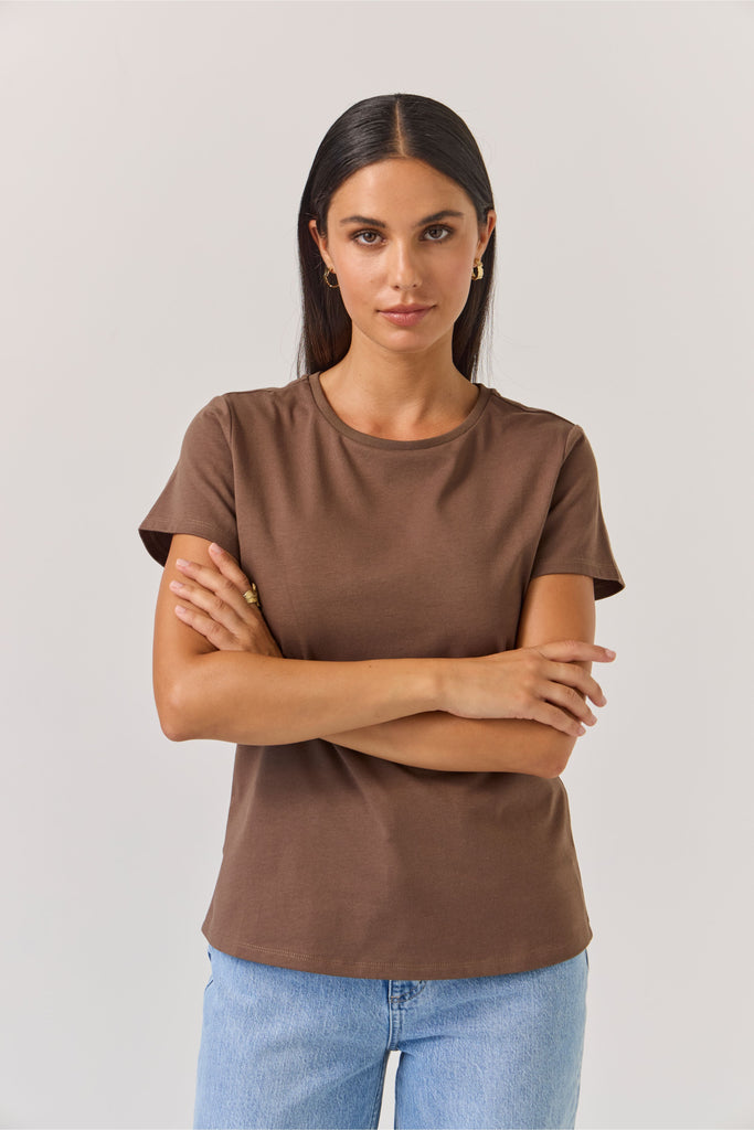 Woman wearing a brown t-shirt and blue jeans against a plain background. Tuesday Label Essential tee in Chocolate.