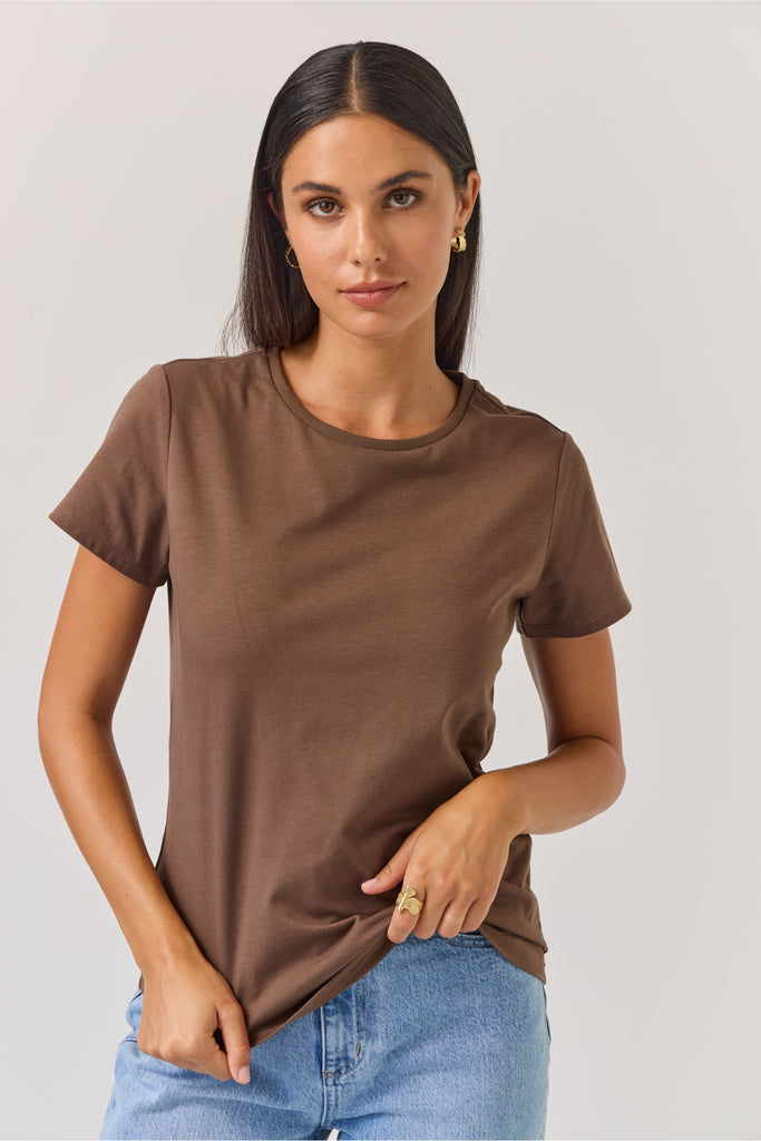 Woman wearing a brown t-shirt and blue jeans against a plain background. Tuesday Label Essential tee in Chocolate.