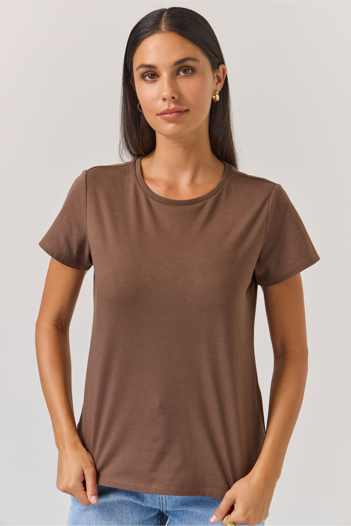 Woman wearing a brown t-shirt and blue jeans against a plain background. Tuesday Label Essential tee in Chocolate.