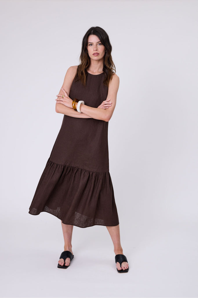 Woman wearing a brown dress with ruffled hem on a white background. Marlow Verona Linen Dress in Carob.