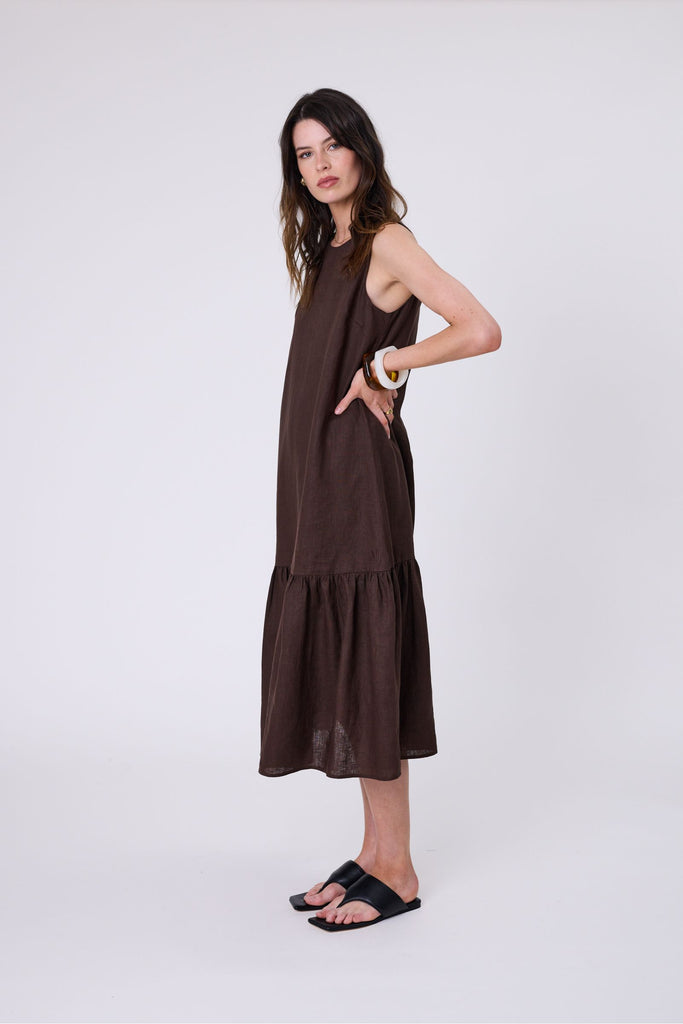 Woman wearing a brown dress with ruffled hem on a white background. Marlow Verona Linen Dress in Carob.