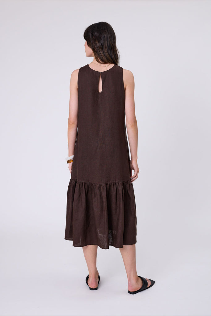 Woman wearing a brown dress with ruffled hem on a white background. Marlow Verona Linen Dress in Carob.