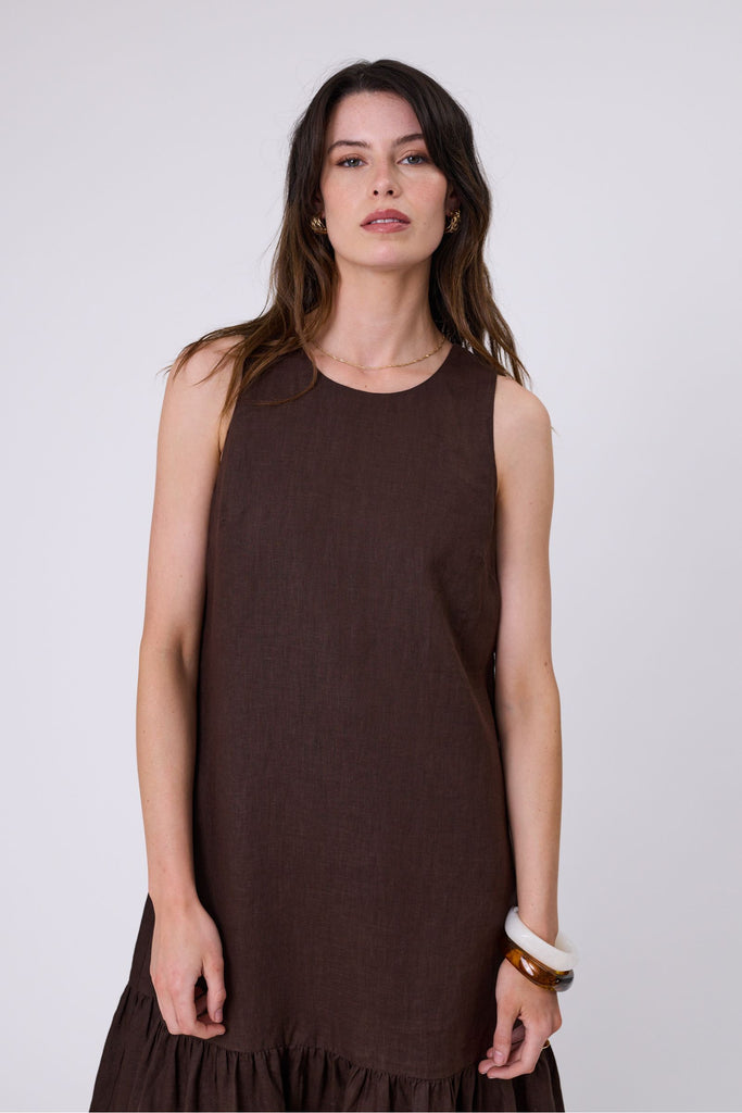 Woman wearing a brown dress with ruffled hem on a white background. Marlow Verona Linen Dress in Carob.