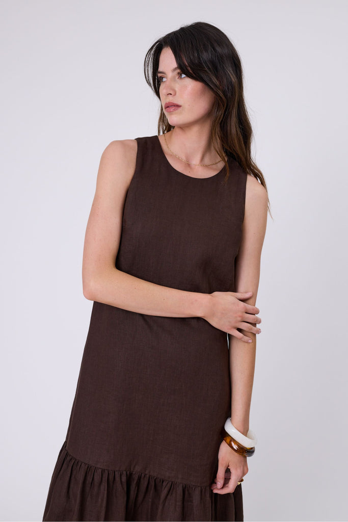 Woman wearing a brown dress with ruffled hem on a white background. Marlow Verona Linen Dress in Carob.
