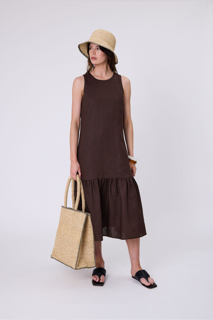 Woman wearing a brown dress with ruffled hem on a white background. Marlow Verona Linen Dress in Carob.