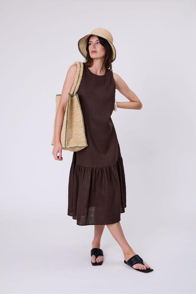Woman wearing a brown dress with ruffled hem on a white background. Marlow Verona Linen Dress in Carob.