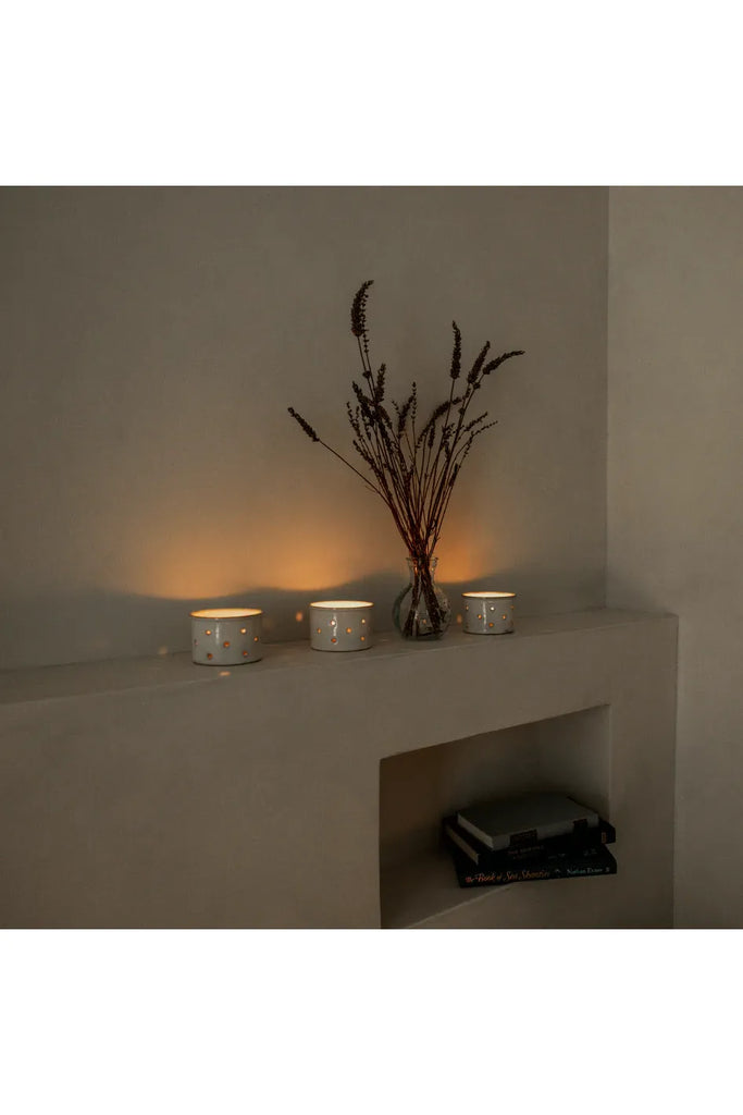 Three small candles and a vase with dried flowers on a concrete surface against a plain wall.