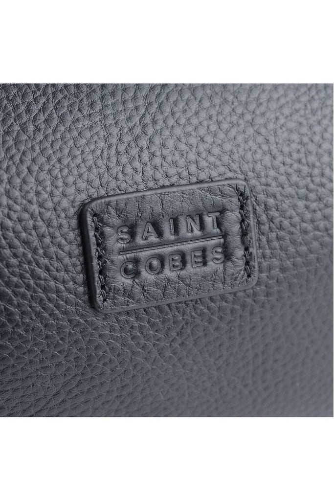 Saint Cobes Close-up of a textured black leather surface of the long haul toiletry/washbag showing the 'Saint Cobes' branding.