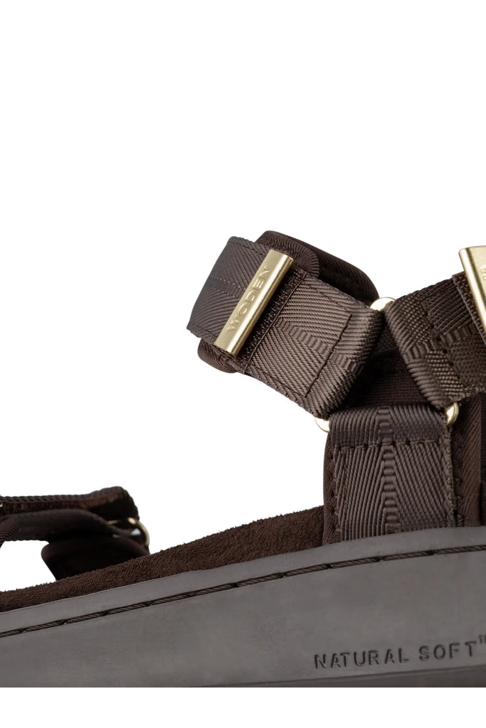 Brown sandal with gold accents on a white background. Woden Line Sandal in Chocolate.
