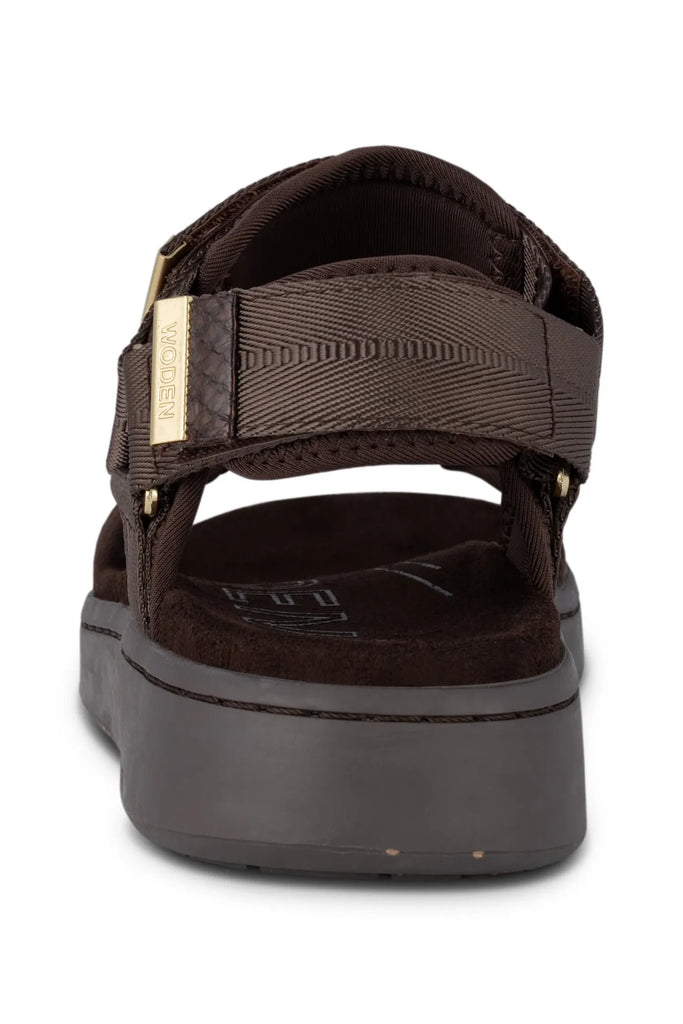 Brown sandal with gold accents on a white background. Woden Line Sandal in Chocolate.