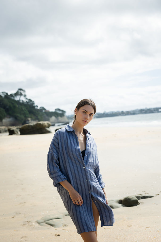 Woman wearing a blue striped shirt dress at the beach. Sophie Always Shirt dress in Denim Stripes.