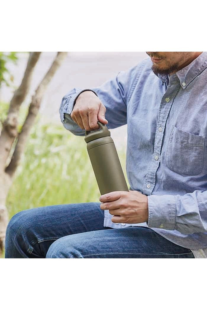 Kinto Day of Tumbler: Khaki Green insulated tumbler with handle. A man sits outdoors holding the insulated tumbler, surrounded by greenery.