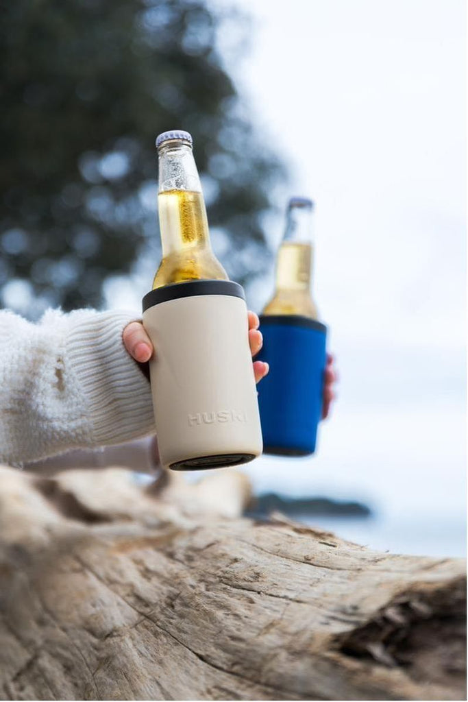 The Limited Edition Ocean Collection Huski Beer Coolers in Sand Beige and Ocean Blue beautifully showcase bottles of refreshing beer, perfectly complemented by a stunning piece of driftwood. 