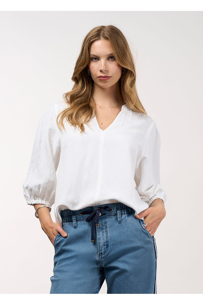Woman wearing a white blouse and blue jeans against a plain background. Madly Sweetly Octave Top in White.