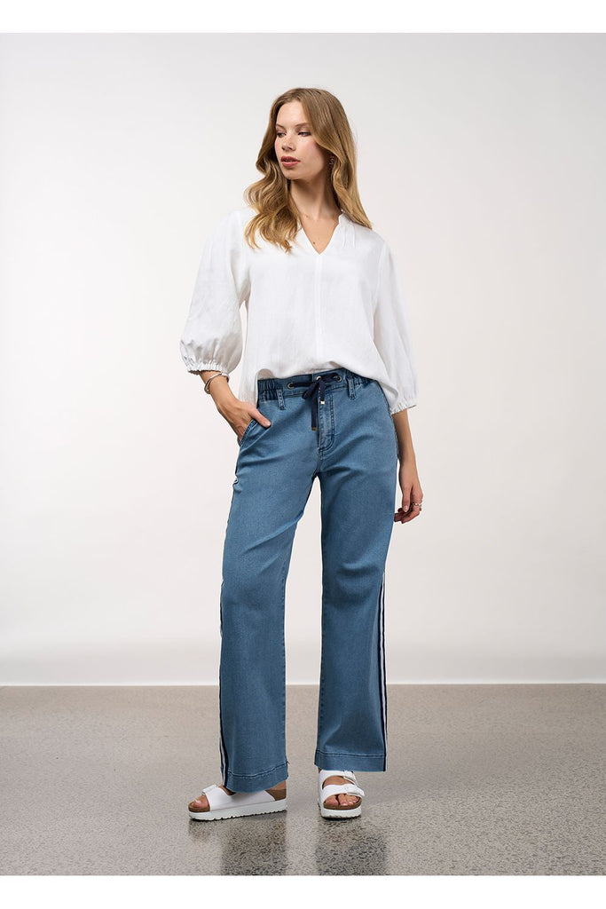 Woman wearing a white blouse and blue jeans against a plain background. Madly Sweetly Octave Top in White.
