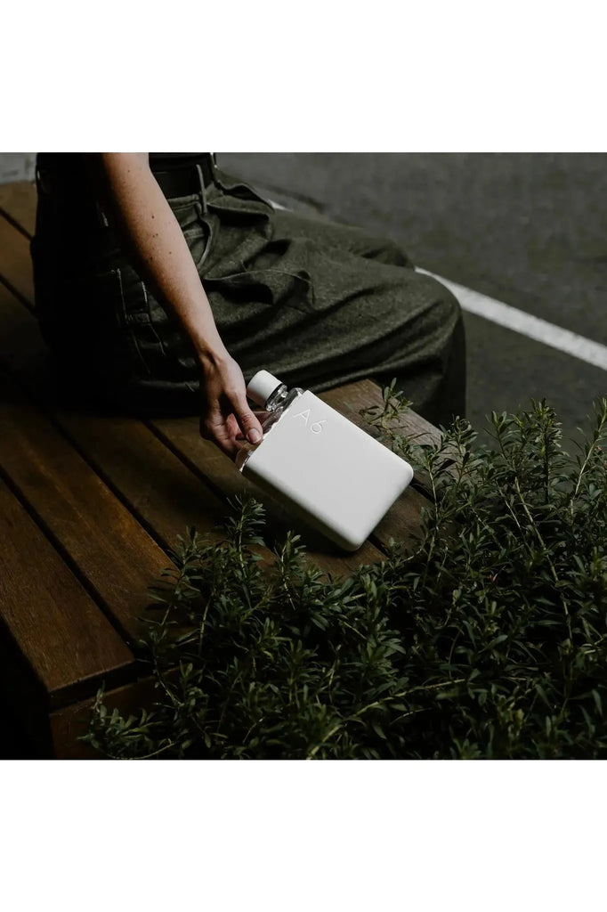 memobottle_A6_bottle_cool_grey_silicone_Sleeeve._Image_shows_bottle_sitting_on_wooden_bench_seat_beside_a_women.