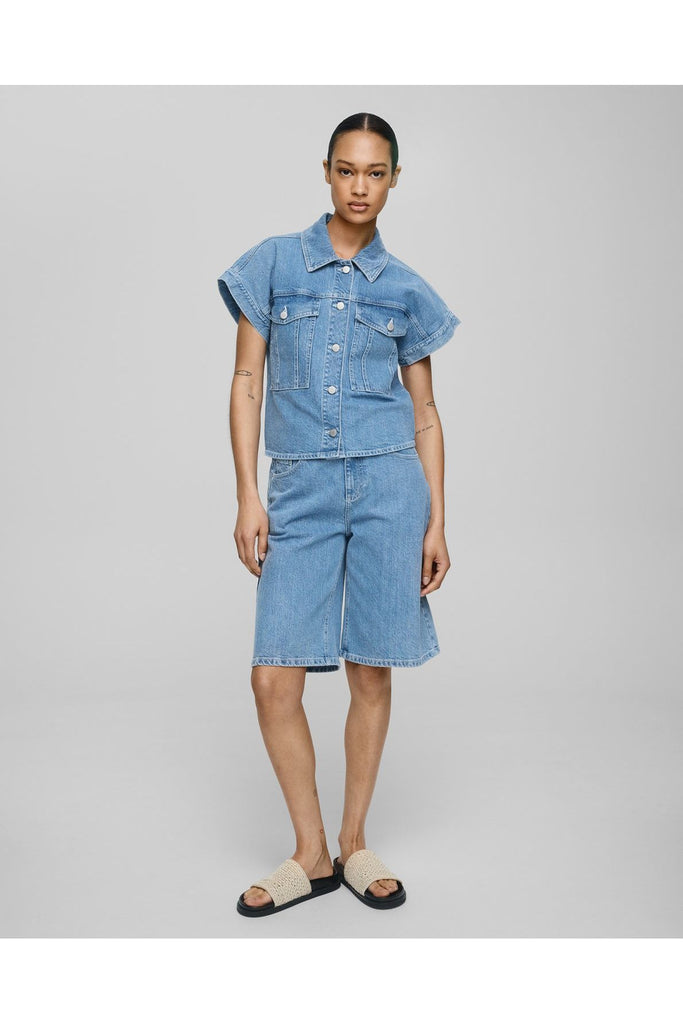 Person wearing a denim outfit with a top and shorts on a grey background. MSCH Elida Ada Denim Bermuda Shorts.