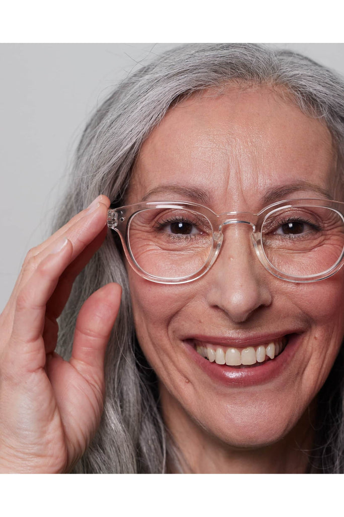 Izipizi Reading Glasses #C Crystal Frame. Clear eyeglasses. Women with grey hair wearing the glasses, smiling against a plain background.