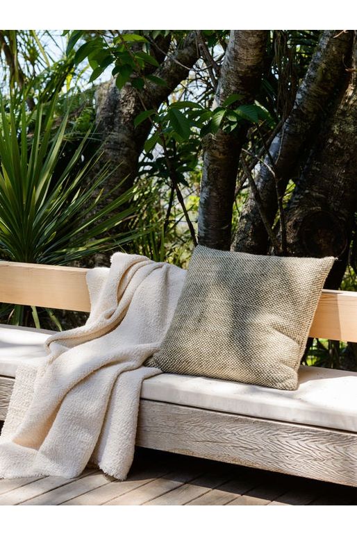 Citta Hutt Wool Cushion in Ivy placed on an outdoor seating squab next to the Citta Boucle Throw