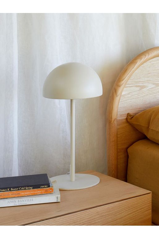 Citta Moon Table Lamp in Bone sitting on a wooden bedside table with some books stting alongside it.