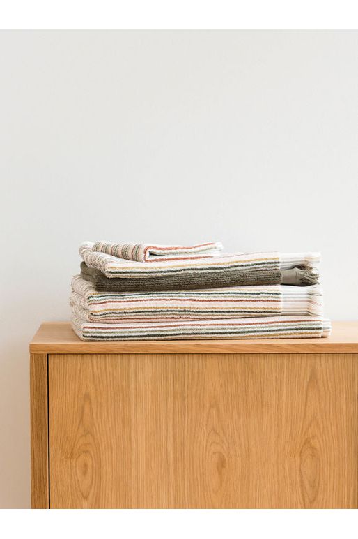 Citta Ribbed Ivy Hand Towel sitting amongst a stack of Alice Cotton Moss/Multi Coloured towels