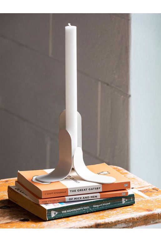 Citta Mild powder coated steel Melt Candle Holder in Bone shown siting of a pile of classic books displaying a white candle