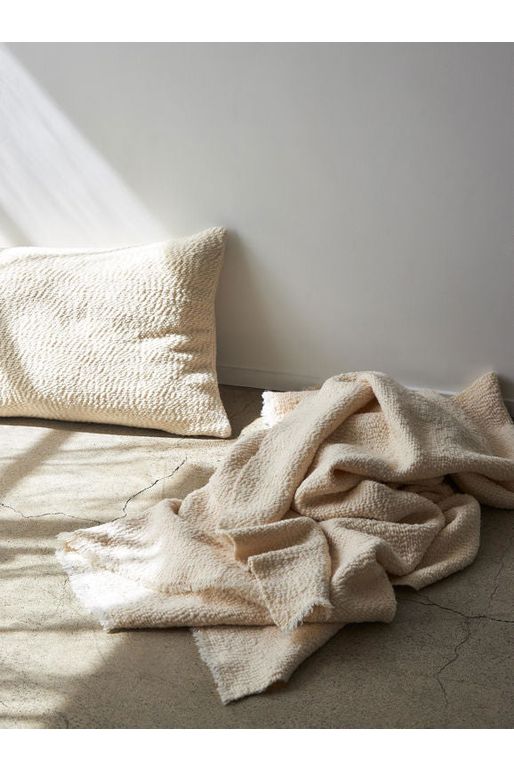 Rectangular Natural Boucle Cushion shown sitting on a concrete floor beside a Natural Boucle Throw