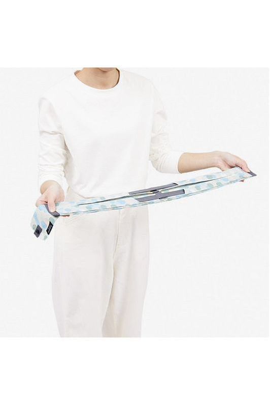 The Shupatto Compact Medium Reusable Shopping Bag in Arare features a hailstone pattern in light blue, sage green, cream, and grey handles. A person is shown holding the bag, which can be compressed and then pulled straight to roll into a small cylindrical shape for easy storage. 