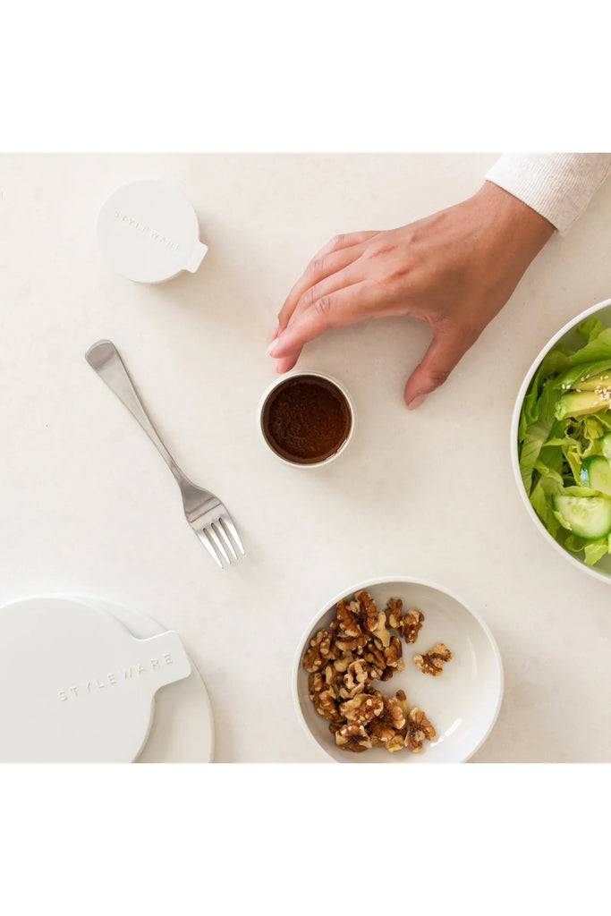 A hand reaches for a mini Styleware container of dressing on a table, alongside a salad and walnuts in two other Dune-coloured Styleware bowls.
