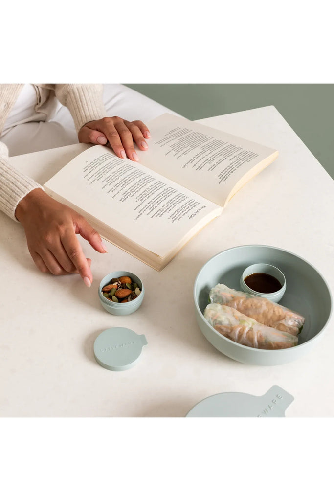 Person reading a book with Styleware's Eculyptus Green lunch bowls filled with food on a table