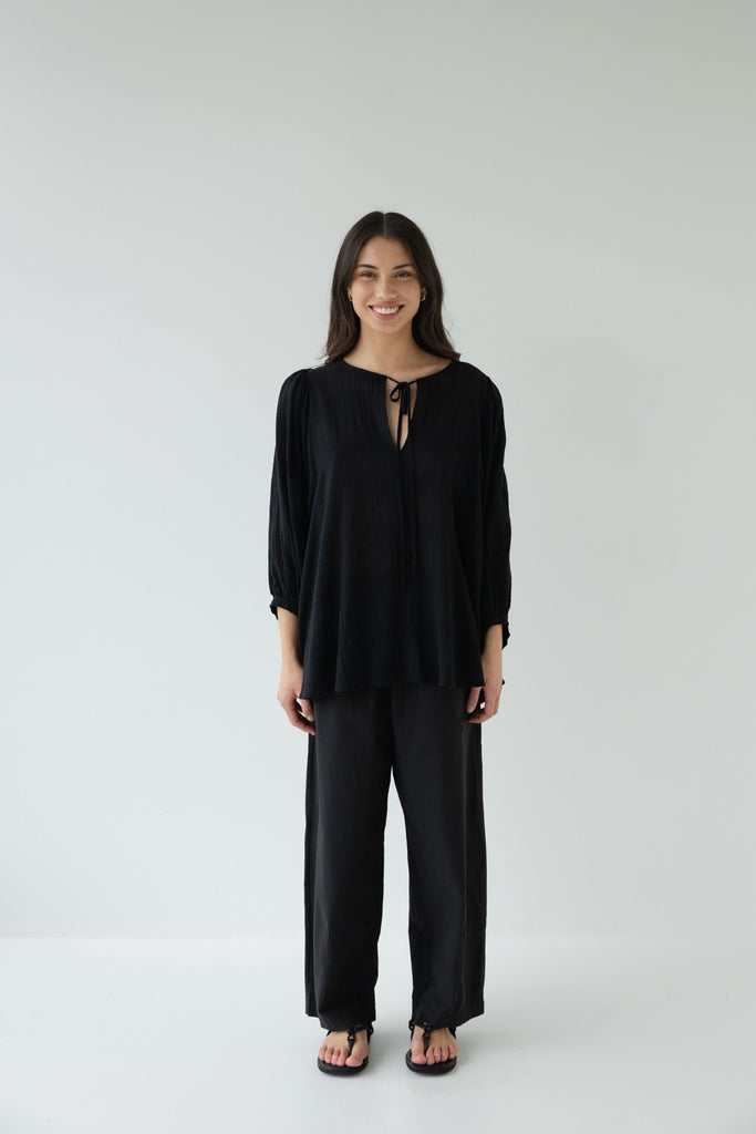 Woman wearing a black outfit on a white background. Sophie Tie Top in black Check.