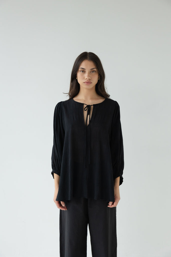 Woman wearing a black outfit on a white background. Sophie Tie Top in black Check.