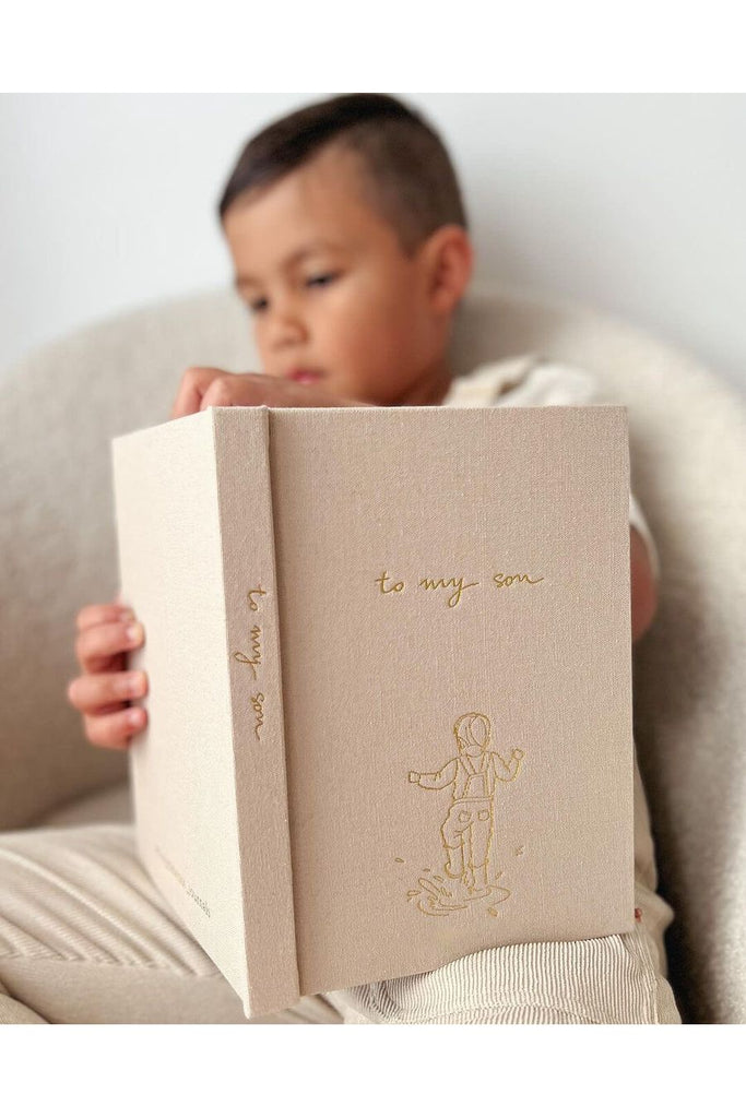 Child sitting and holding Forget Me Not's Keepsake Journal with fabric Latte cover To My Son 