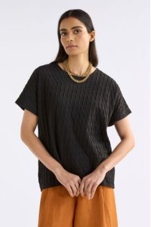 Woman wearing an Elk black textured top and orange pants on a white background