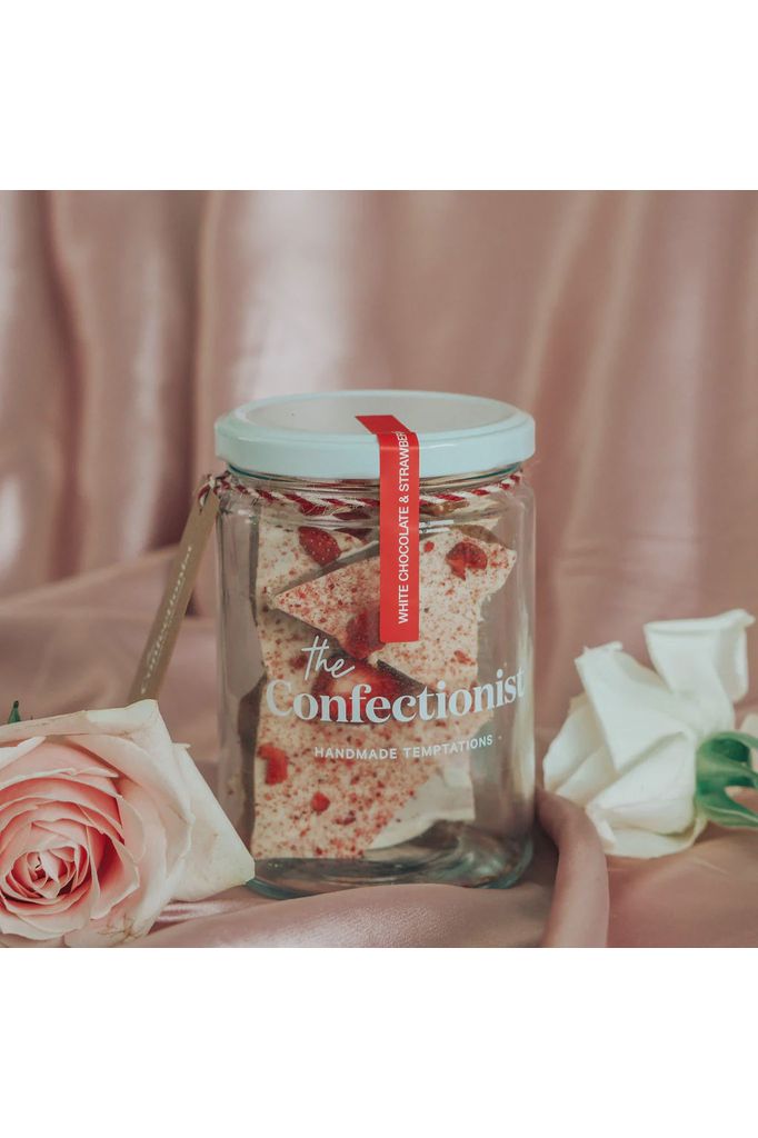 the Confectionish Handmade White Chocolate and Strawberry Toffee photo of Jar sitting amongst folds of pink satin with pink and white roses