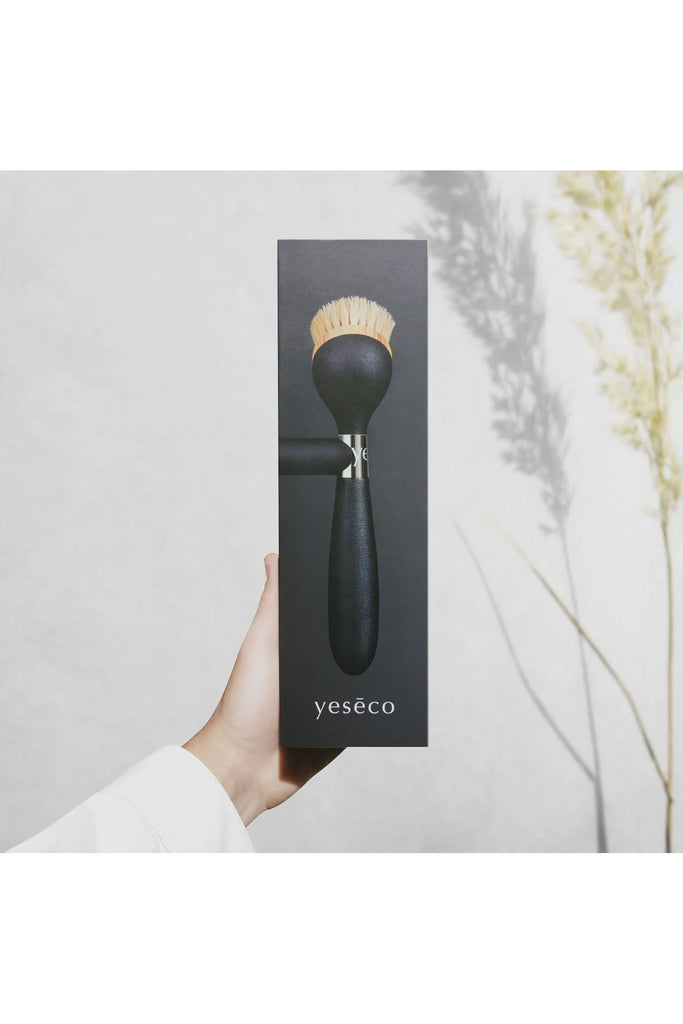 Yeseco.life One Brush The Ultimate Dish Brush Black Handle. Outer Packaging being held up by a human hand. Packaging shows photo of the actual Dish Brush Handle and Head and Magnetic Stand. 